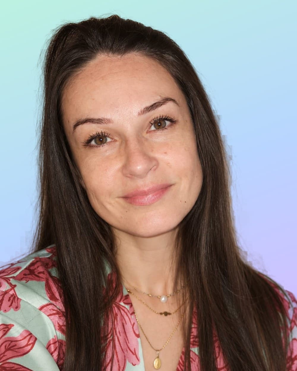 Ingrid, souriante, cheveux longs bruns, chemise fleurie, sur un fond dégradé menthe et lavande